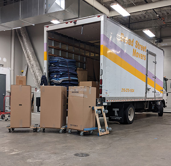 A truck from Broad Street Movers parked inside a warehouse during a local commercial move with several tall boxes sitting on dollies after being unloaded from the truck
