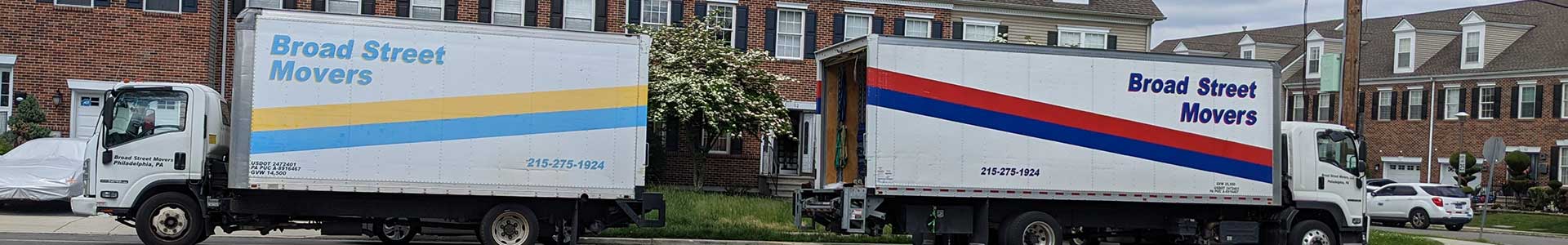 Two different-sized trucks from Broad Street Movers parked outside apartment complex in Philly