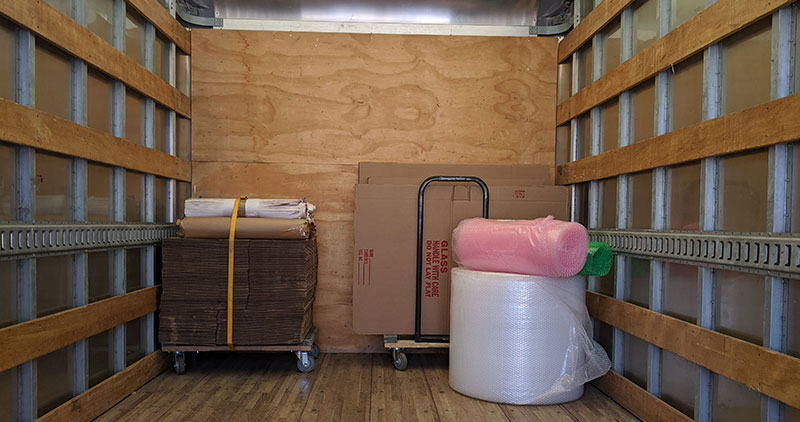 The rear-view of a clean truck-bed from a Broad Street Movers moving truck, with various packaging materials inside