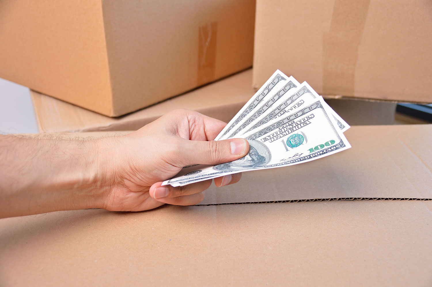 A hand holding money over moving boxes while evaluating the costs of moving in Philly
